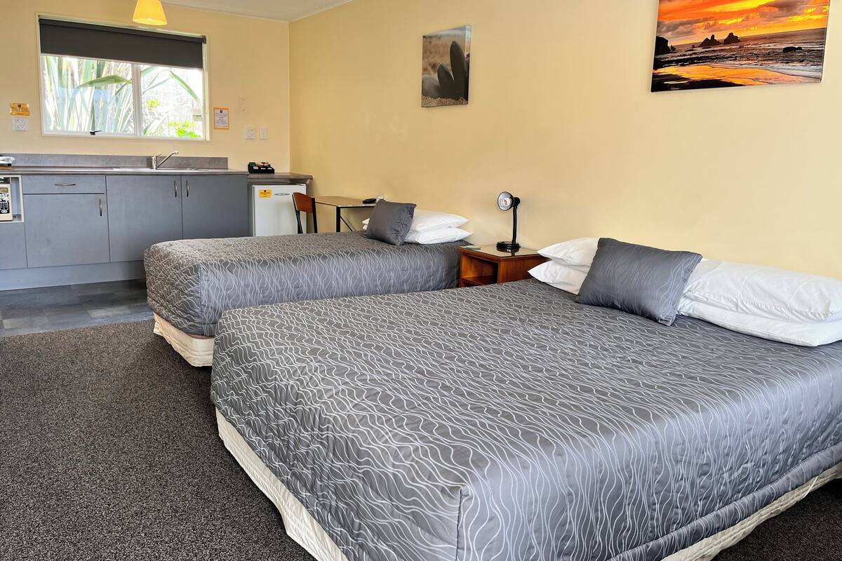 A hotel room with two beds, a small kitchenette, a window with a view, and a painting on the wall.