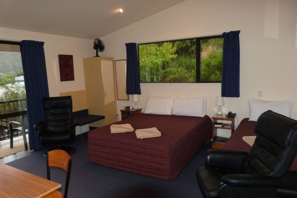 A hotel room with a large bed, two chairs, a desk, a wardrobe, and a window with curtains.