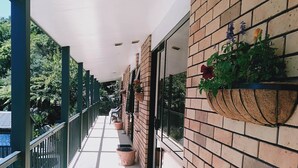 A covered outdoor balcony with a tiled floor, potted plants, and a brick wall. - Sundowner Motel (Greymouth)