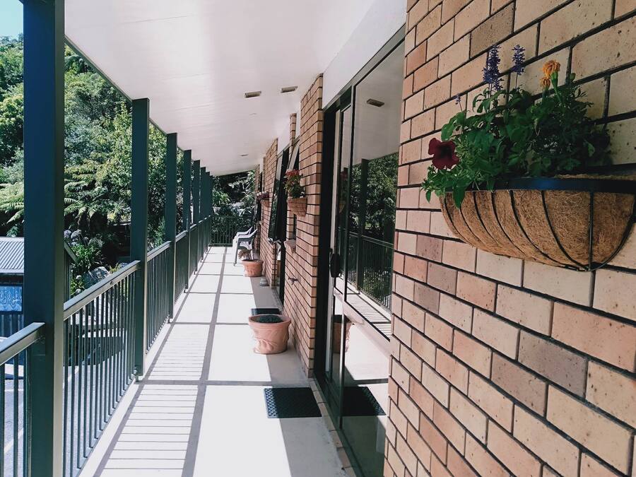 Un balcón techado al aire libre con suelo de baldosas, plantas en macetas y una pared de ladrillo.