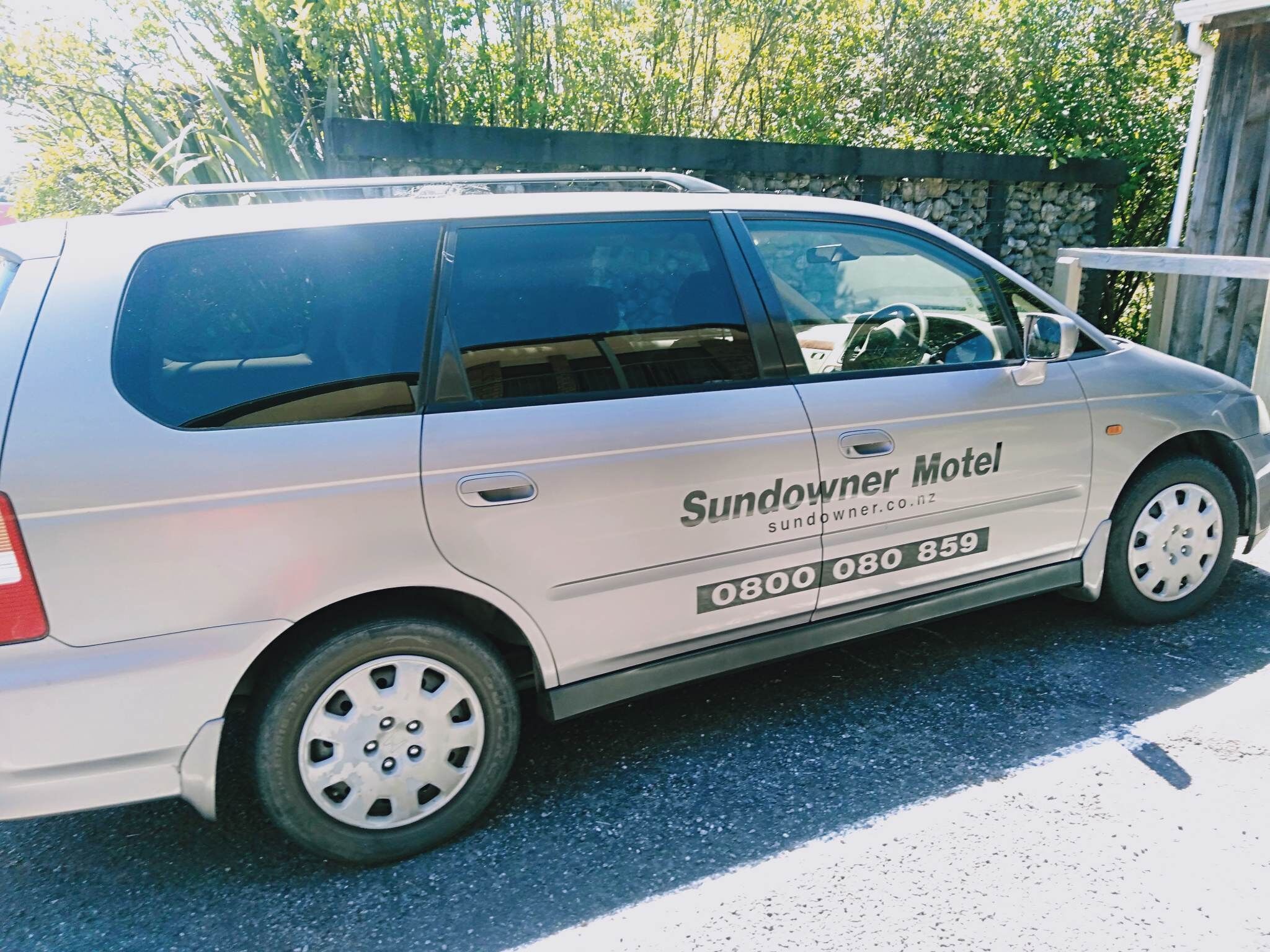 Un fourgon blanc avec l’inscription « Sundowner Motel » et un numéro de téléphone sur le côté.