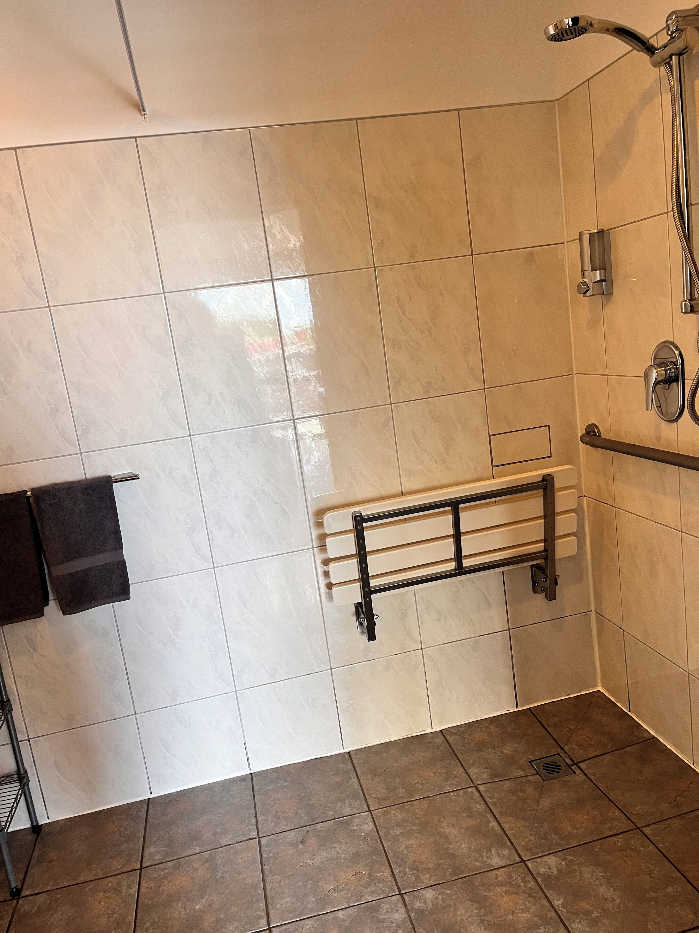 A bathroom with beige tiled walls, a shower area with a handheld showerhead, a towel rack, and a floor drain.