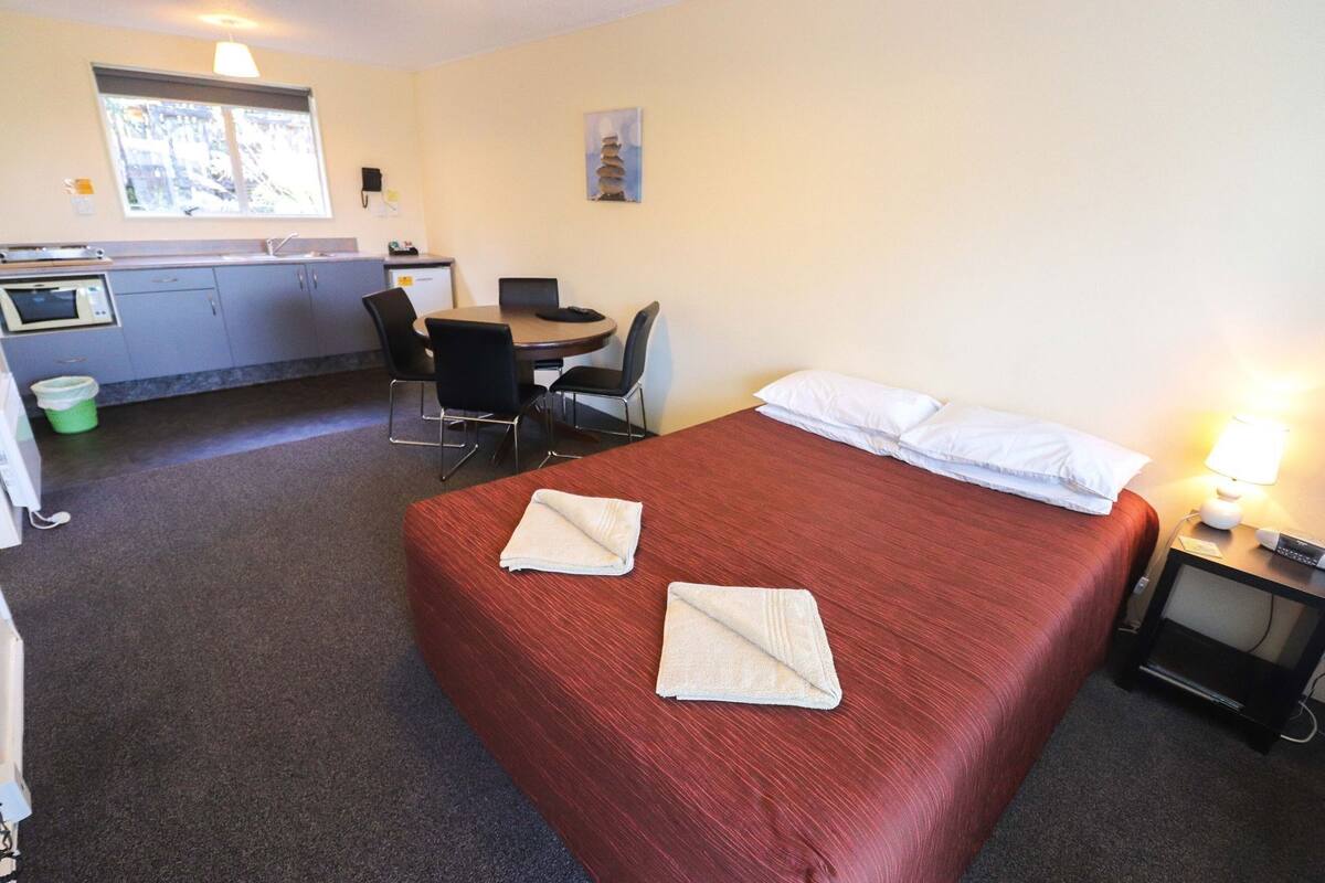 A hotel room with a bed, a desk, a chair, a microwave, and a sink.