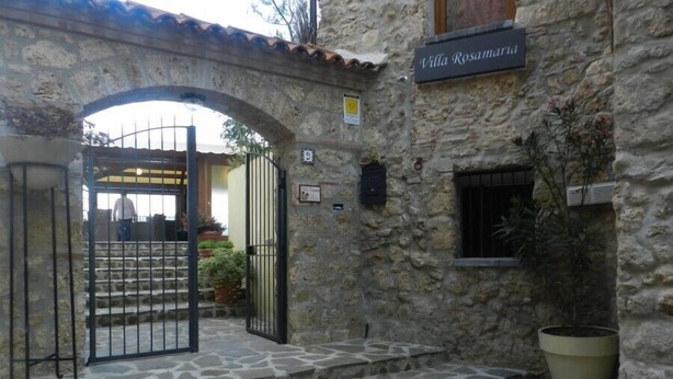 A stone building with a sign reading "Villa Rosamart." There are stone steps leading to a gated entrance, a potted plant, and a small window. - Villa RosaMaria (San Chirico Raparo)