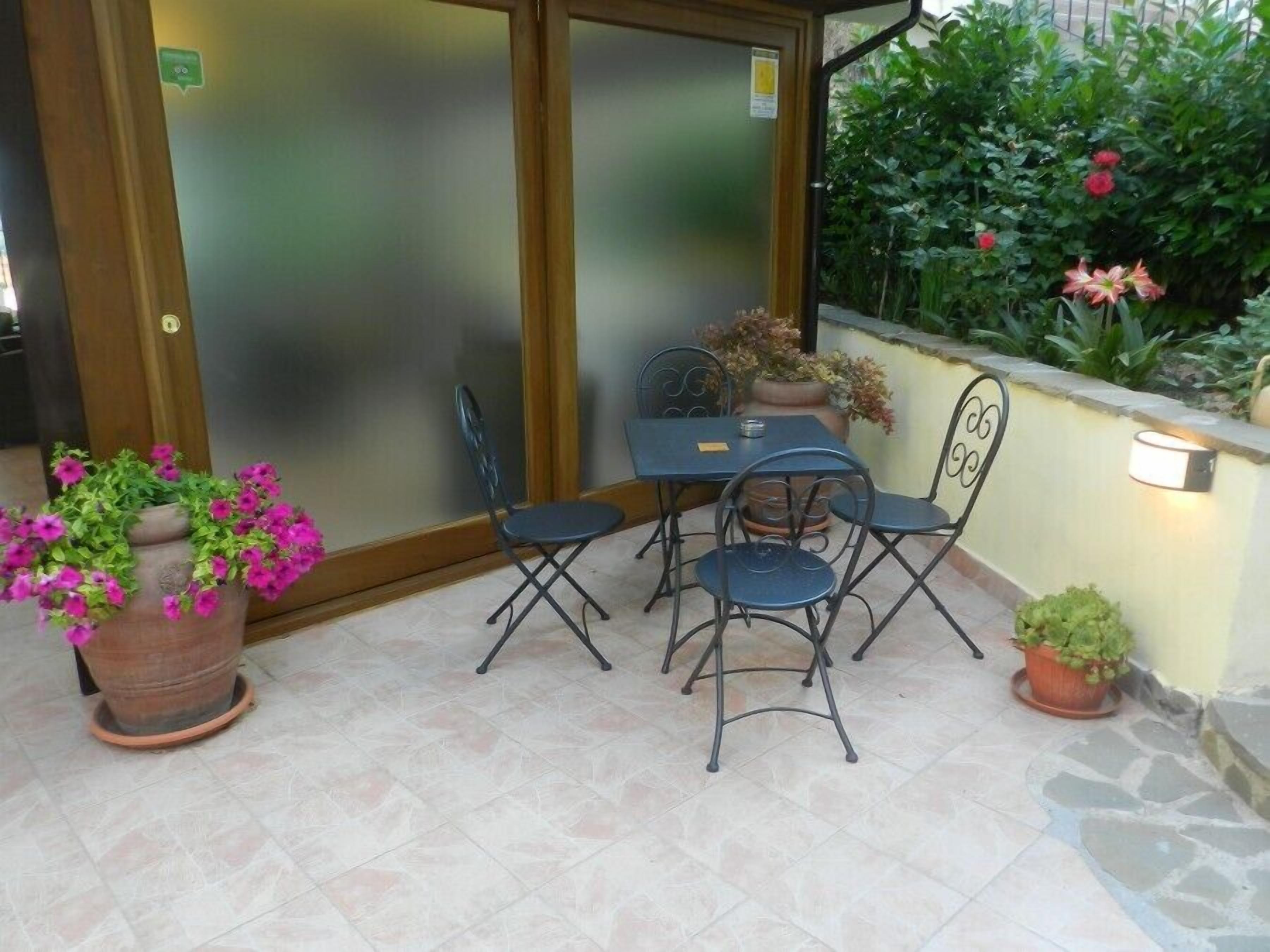 Un patio con mesa y sillas, plantas en macetas y una puerta con paneles de vidrio esmerilado.