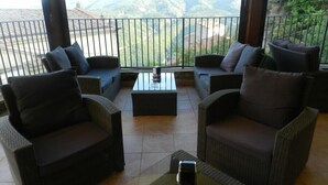 A balcony with wicker furniture and a glass table, overlooking a mountainous landscape. - Villa RosaMaria (San Chirico Raparo)