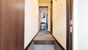 Un estrecho pasillo con una puerta de madera a la izquierda y suelo de baldosas.