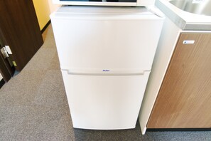 Un refrigerador blanco y compacto con un microondas incorporado encima, situado en una cocina con armarios de madera y alfombra gris.