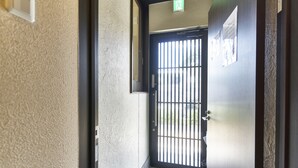 Un pasillo con una puerta que incluye una reja de seguridad metálica, un interruptor de luz y una pequeña señal sobre la puerta.