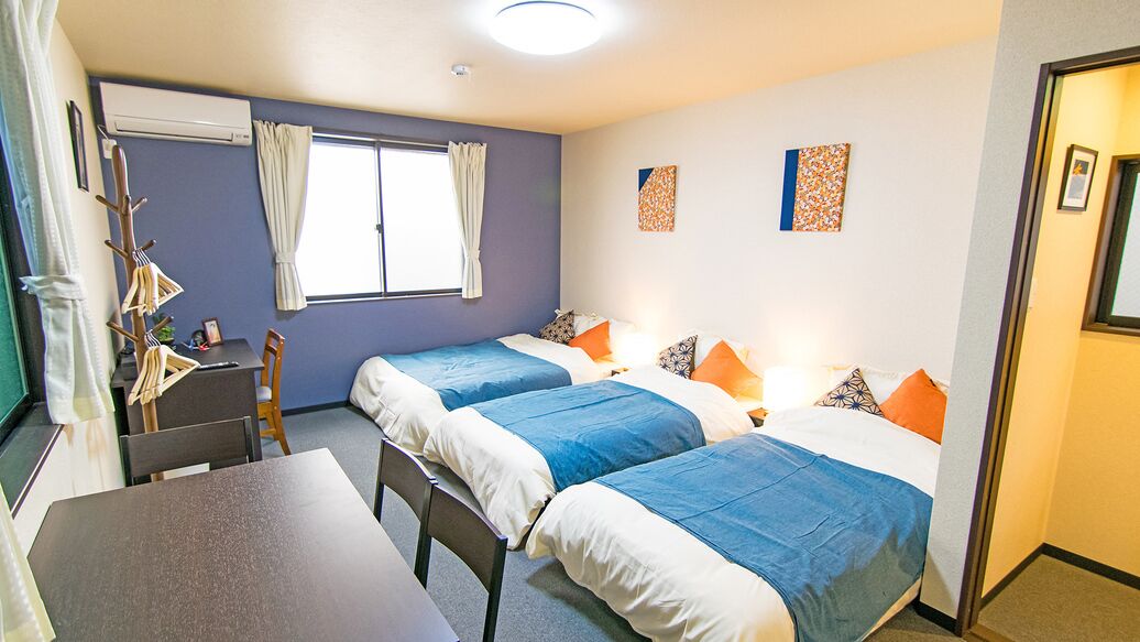 A room with two beds, a table, chairs, and a window with curtains.