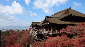 Edificio japonés tradicional de estructura de madera y techo de paja, rodeado de follaje otoñal.