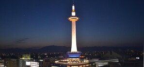 Una torre alta con un mirador circular en la parte superior, rodeada de edificios iluminados y una cadena montañosa al fondo.