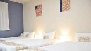 Habitación de hotel con tres camas, cada una con ropa blanca y almohadas decorativas. Hay lámparas de pared sobre las camas.