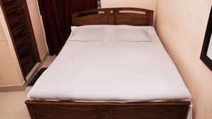 A single bed with a wooden frame and white bedding in a room with a tiled floor and a wooden door. - Hotel Diamond Park (Chittagong)