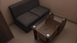 A small room with a dark grey sofa and a glass-top coffee table with wooden legs. - Hotel Diamond Park (Chittagong)