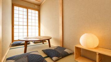 A traditional Japanese room with tatami flooring, a low wooden table, cushions, and a paper lantern.