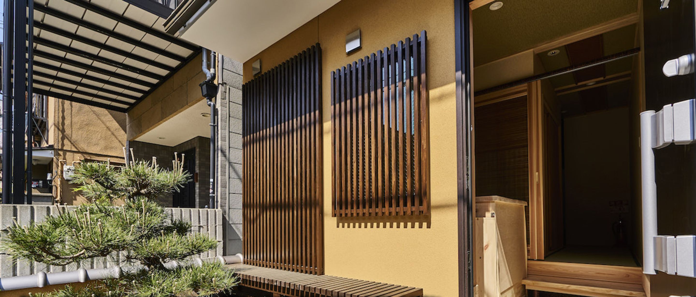 A traditional Japanese building with a wooden exterior, a sliding door, and a small garden area with a pine tree.