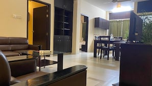 Una sala de estar moderna con un sofá, una mesa de centro y un mueble para la televisión. Se ve un área de cocina con una mesa de comedor y sillas al fondo.