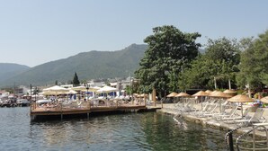 A waterfront hotel with a dock, lounge chairs, umbrellas, and a view of mountains. - Karianda Hotel (Bodrum)