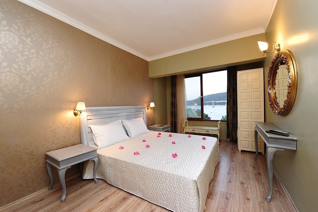 Habitación de hotel con una cama grande, dos mesitas de noche, un tocador, un espejo y una ventana con vistas al exterior.