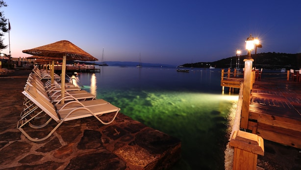 A waterfront area with lounge chairs, a thatched-roof structure, and a wooden dock. - Karianda Hotel (Bodrum)