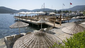 A marina with wooden deck chairs and umbrellas, boats docked, and a mountainous backdrop. - Karianda Hotel (Bodrum)