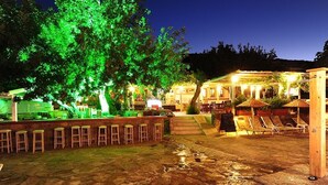 An outdoor bar area with a stone floor, wooden stools, and a covered seating area with umbrellas. - Karianda Hotel (Bodrum)