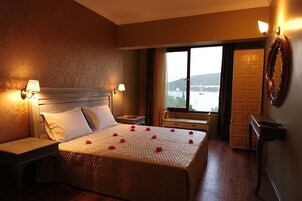 A hotel room with a bed, nightstands, a window with a view, and a door.