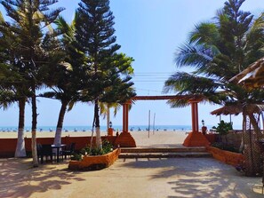 A beachside patio with palm trees, outdoor seating, and a view of the beach. - Divine Eco Resort (Cox's Bazar)