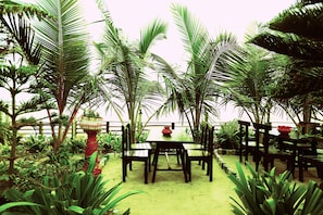 Enjoy a serene meal amidst lush tropical plants and palm trees in this peaceful outdoor dining area.