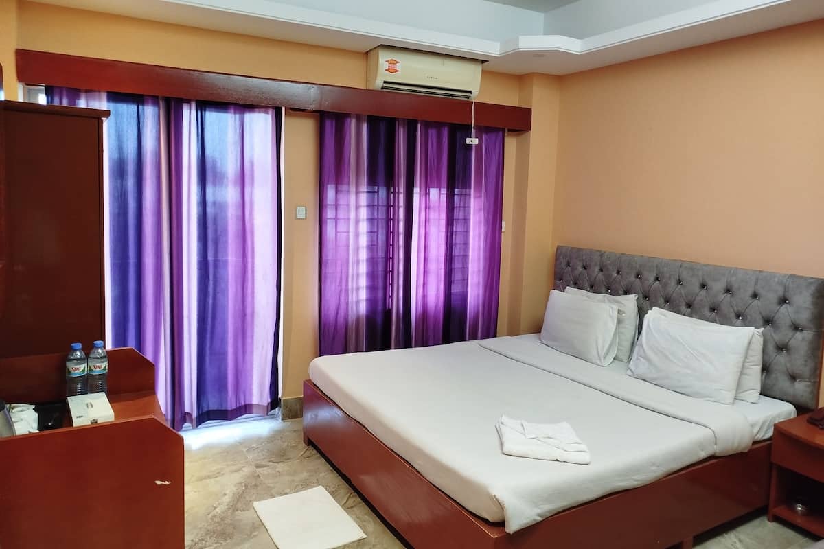 Habitación de hotel con una cama grande, un armario, un escritorio con dos botellas y cortinas moradas.