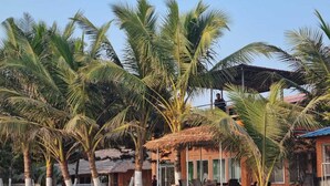 A tropical setting with palm trees and a thatched-roof structure, likely a guest area or reception. - Divine Eco Resort (Cox's Bazar)