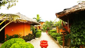 A narrow pathway flanked by lush greenery and traditional thatched-roof buildings. - Divine Eco Resort (Cox's Bazar)