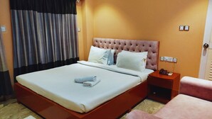 A hotel room with a large bed, a bedside table with a phone, a chair, and a window with curtains. - Divine Eco Resort (Cox's Bazar)