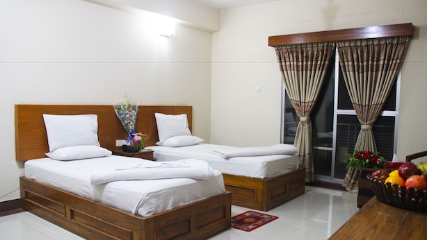 A hotel room with two wooden beds, white bedding, a wooden nightstand, a red rug, and a fruit bowl on the table. - Cox's Hilton (Cox's Bazar)