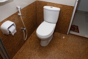A bathroom with a toilet, a paper towel dispenser, and a shower head. - Cox's Hilton (Cox's Bazar)