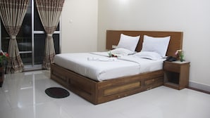 A bedroom with a wooden bed, white bedding, a bedside table with a phone, and a window with curtains. - Cox's Hilton (Cox's Bazar)