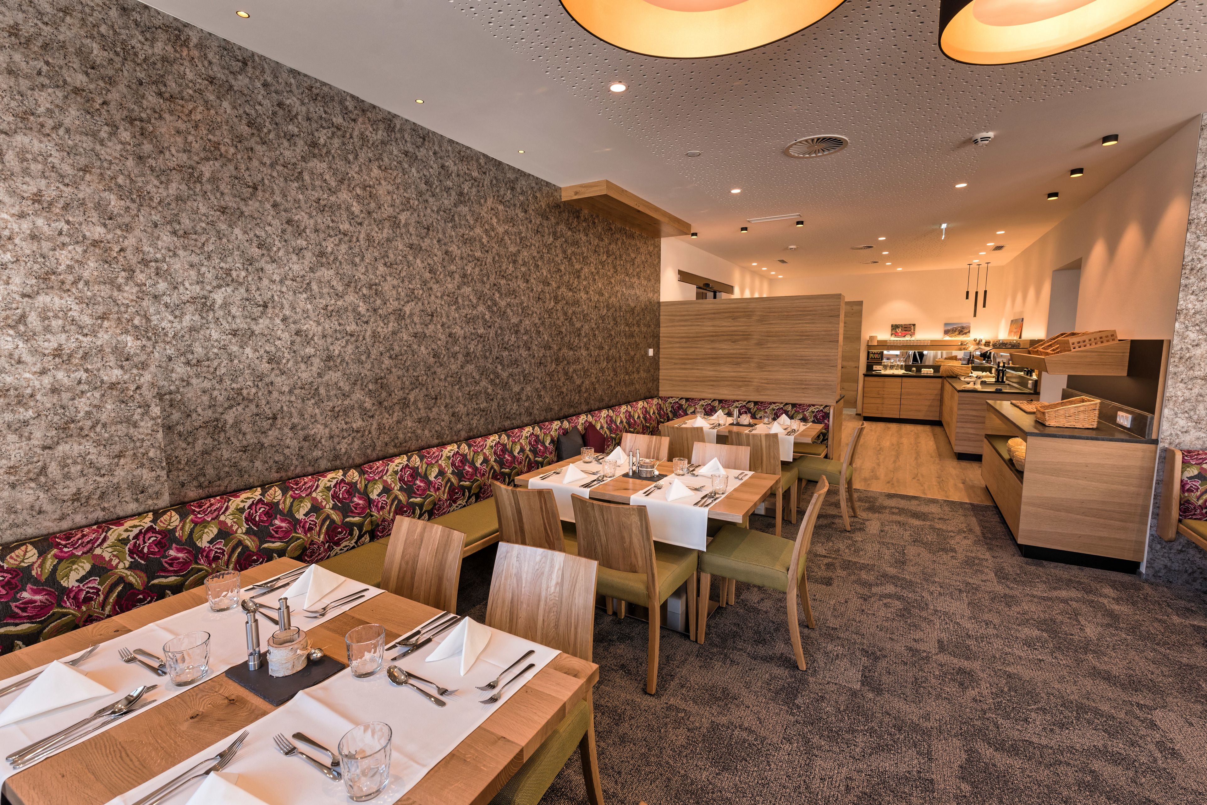 Un restaurant avec des tables et des chaises en bois, un mur décoré de motifs floraux et un sol recouvert de moquette.