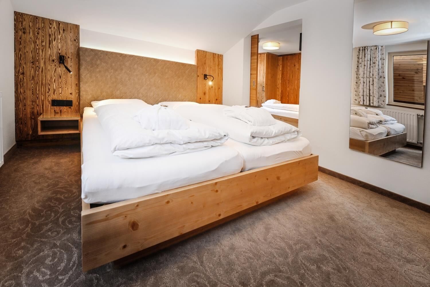 A modern room with a wooden bed, a built-in bench, a mirror, and a wooden wall panel.