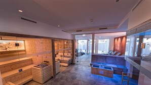 Un moderno espacio de spa con bancos de madera, una sauna con paredes de vidrio y una zona de relajación con azulejos azules.