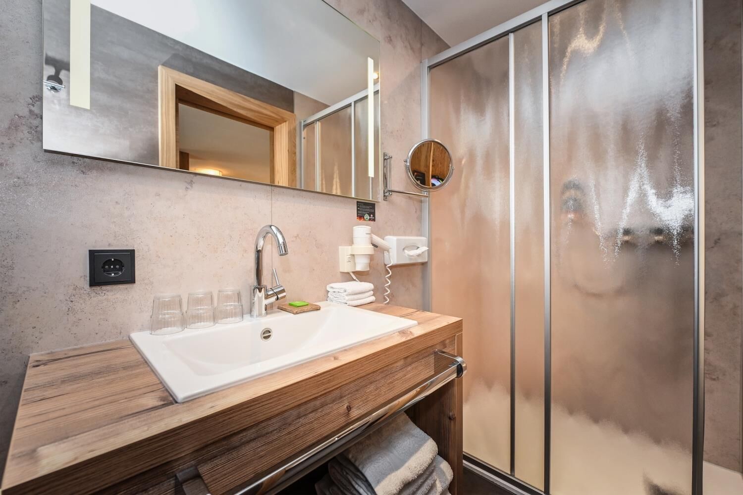 A modern bathroom with a wooden vanity, a large mirror, a shower with a glass door, and a towel rack.