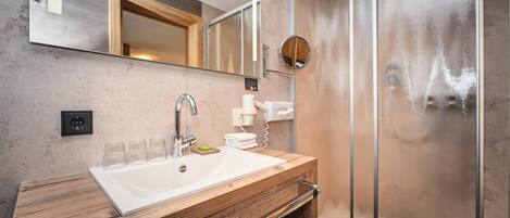 Un baño moderno con tocador de madera, un espejo grande, una ducha con puerta de vidrio y un perchero para toallas.