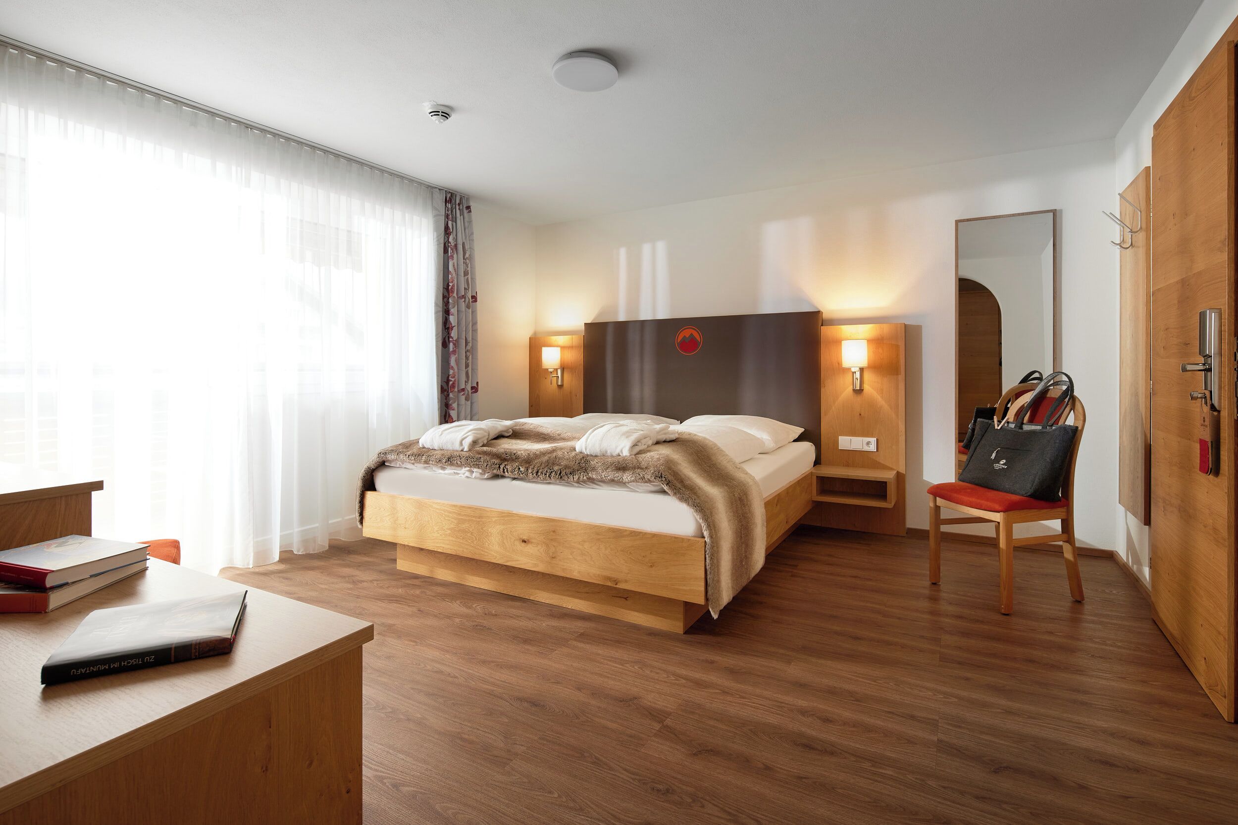 Una camera d'albergo moderna con un letto in legno, lampade ai comodini, una scrivania e una sedia.
