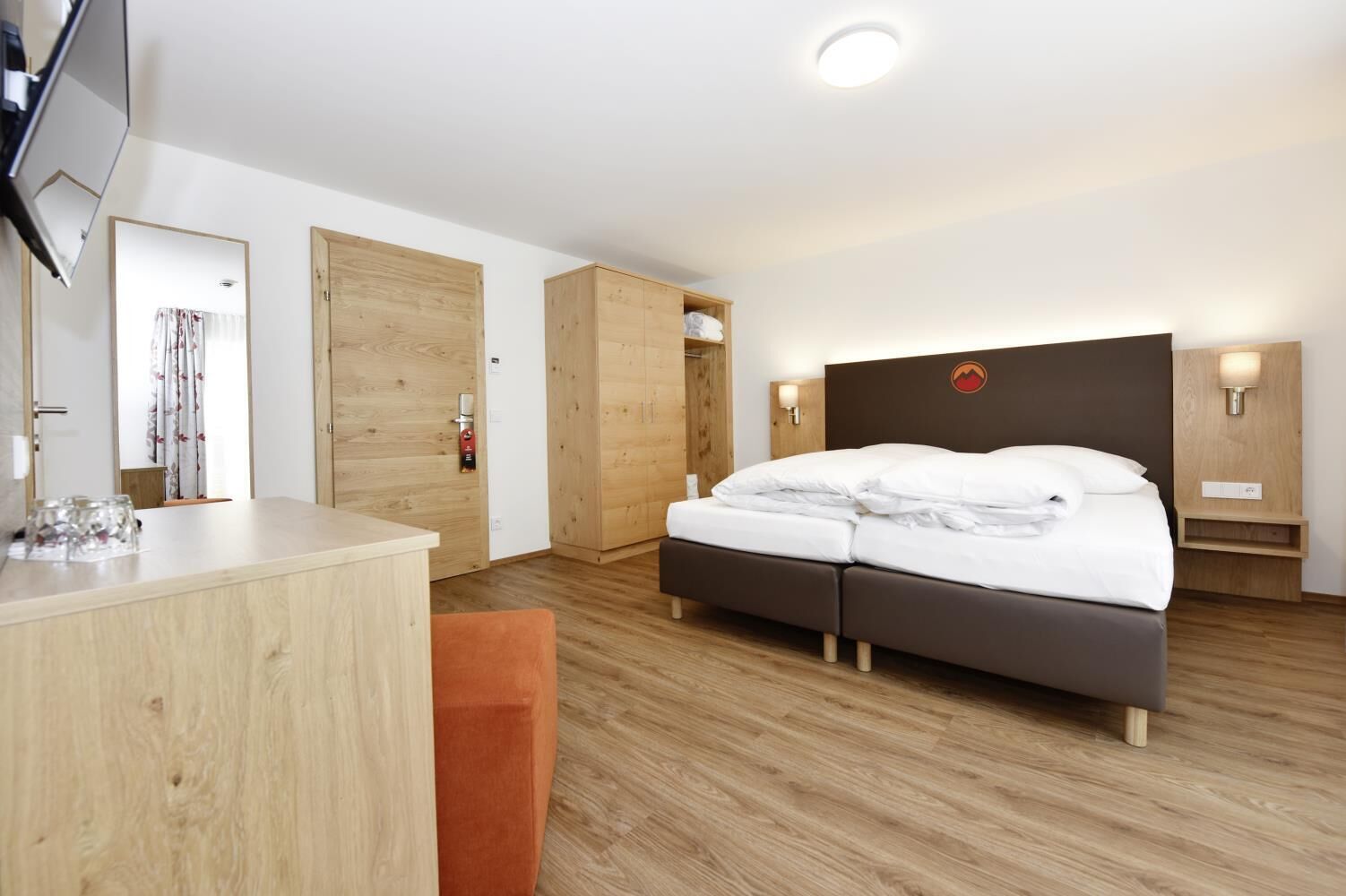 Una habitación de hotel con cama, escritorio, silla, suelo de madera y armario de madera.