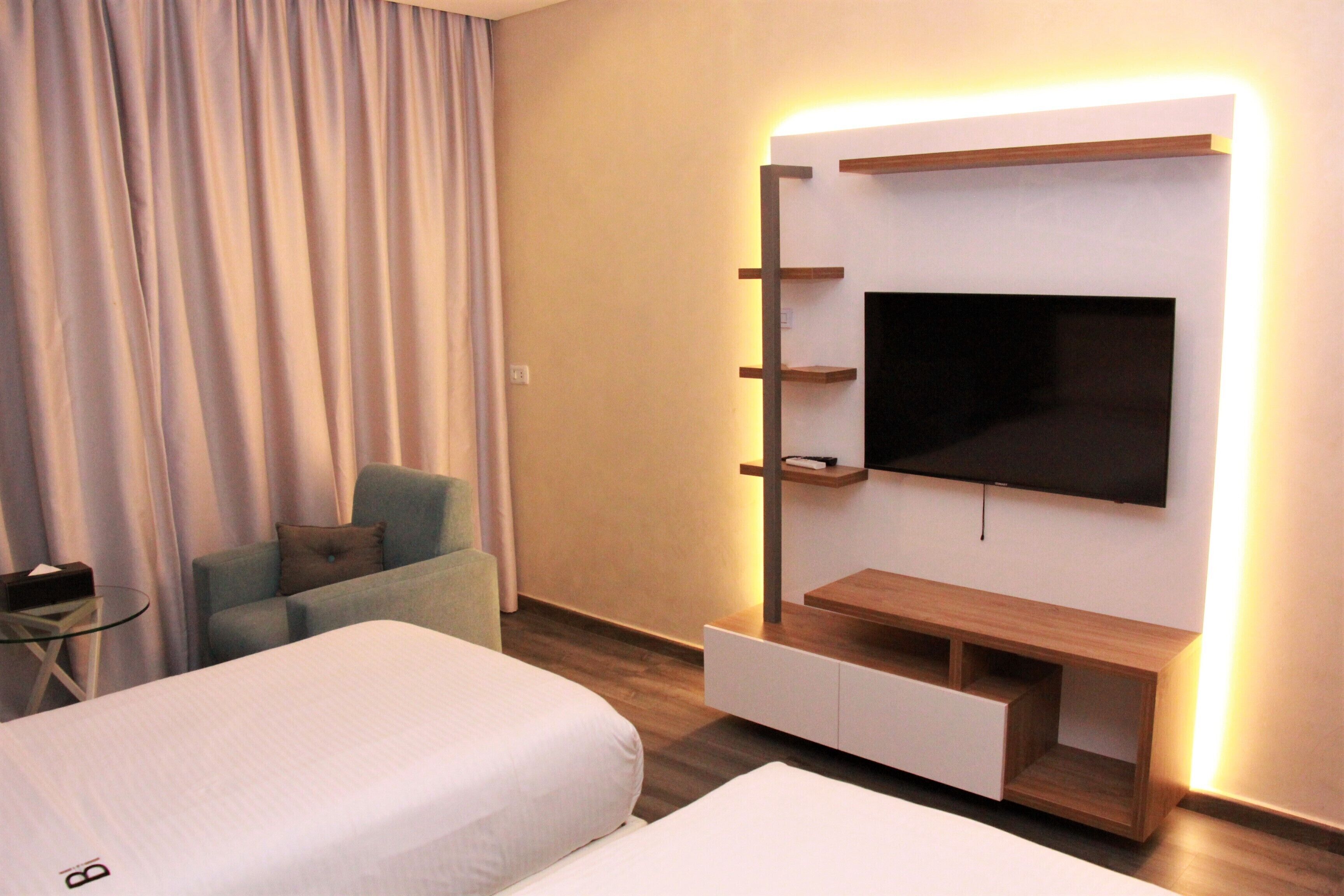Ein Hotelzimmer mit zwei Betten, einem an der Wand montierten Fernseher, einem kleinen Tisch und einem Stuhl.