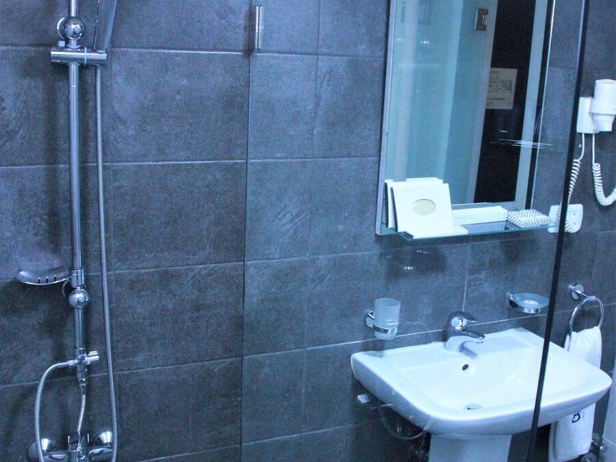Un baño moderno con ducha de vidrio, un lavamanos pedestal blanco y un espejo sobre el lavamanos.