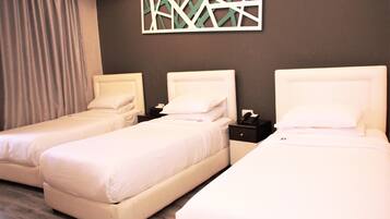 Habitación de hotel con tres camas individuales, una pared de color oscuro y un elemento decorativo geométrico sobre las camas.