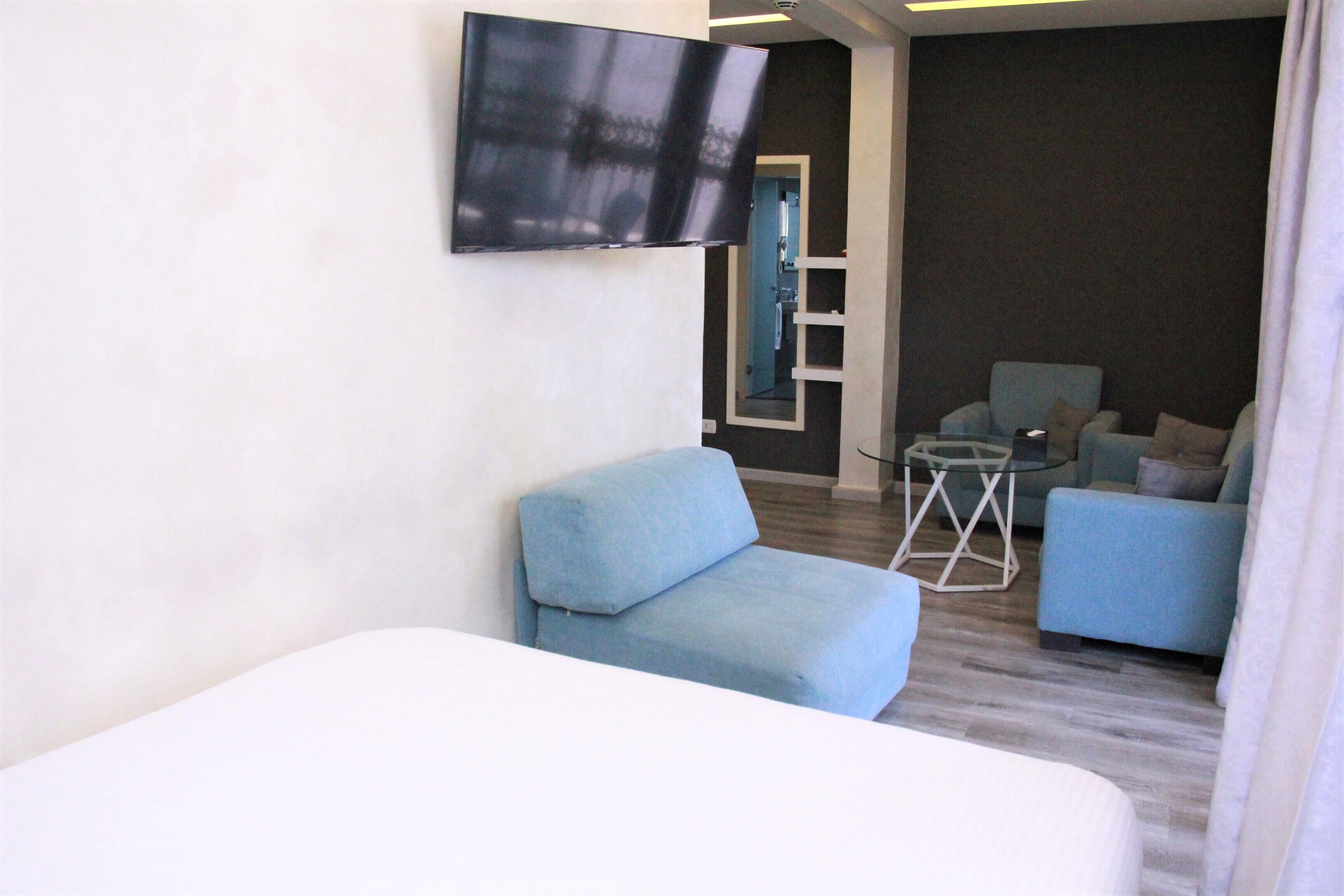 A modern hotel room with a flat-screen TV mounted on the wall, a sofa, a chair, and a small table.