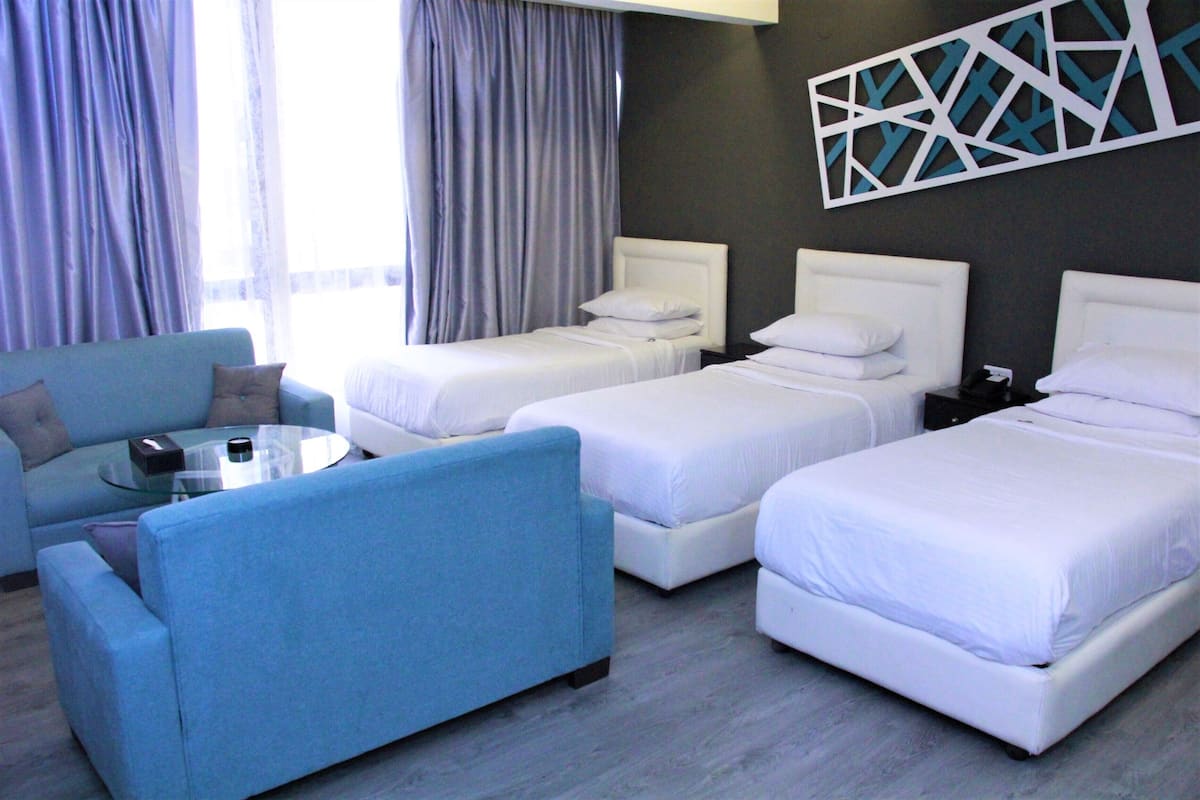 A hotel room with two single beds, a blue sofa, a round glass coffee table, and a modern wall art piece.