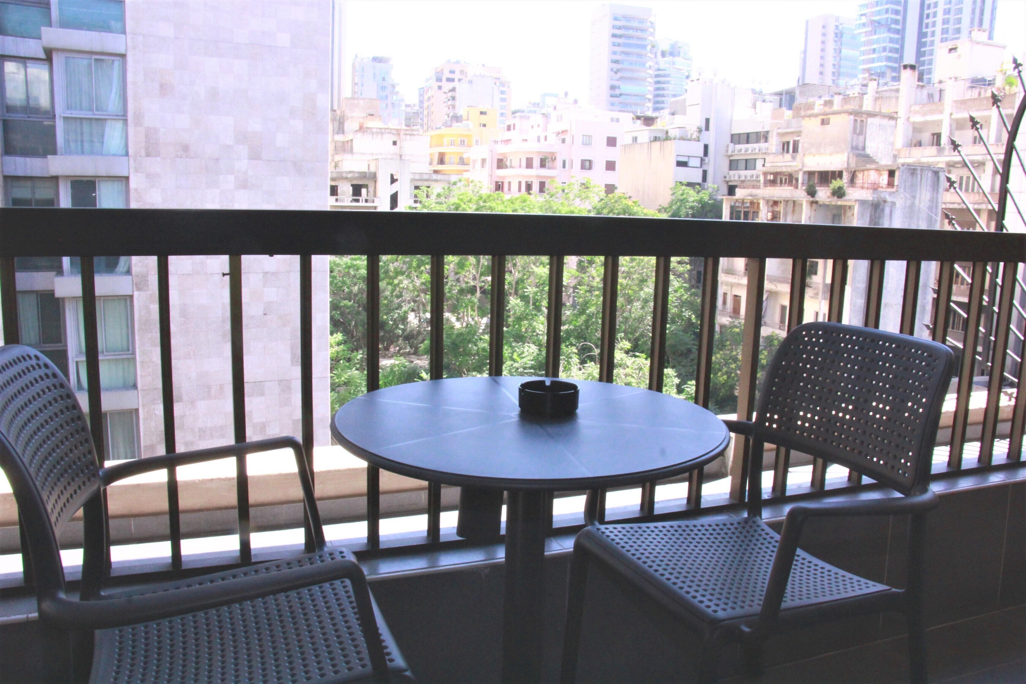Un balcón con una mesa redonda y dos sillas, con vista a un paisaje urbano con diversos edificios.